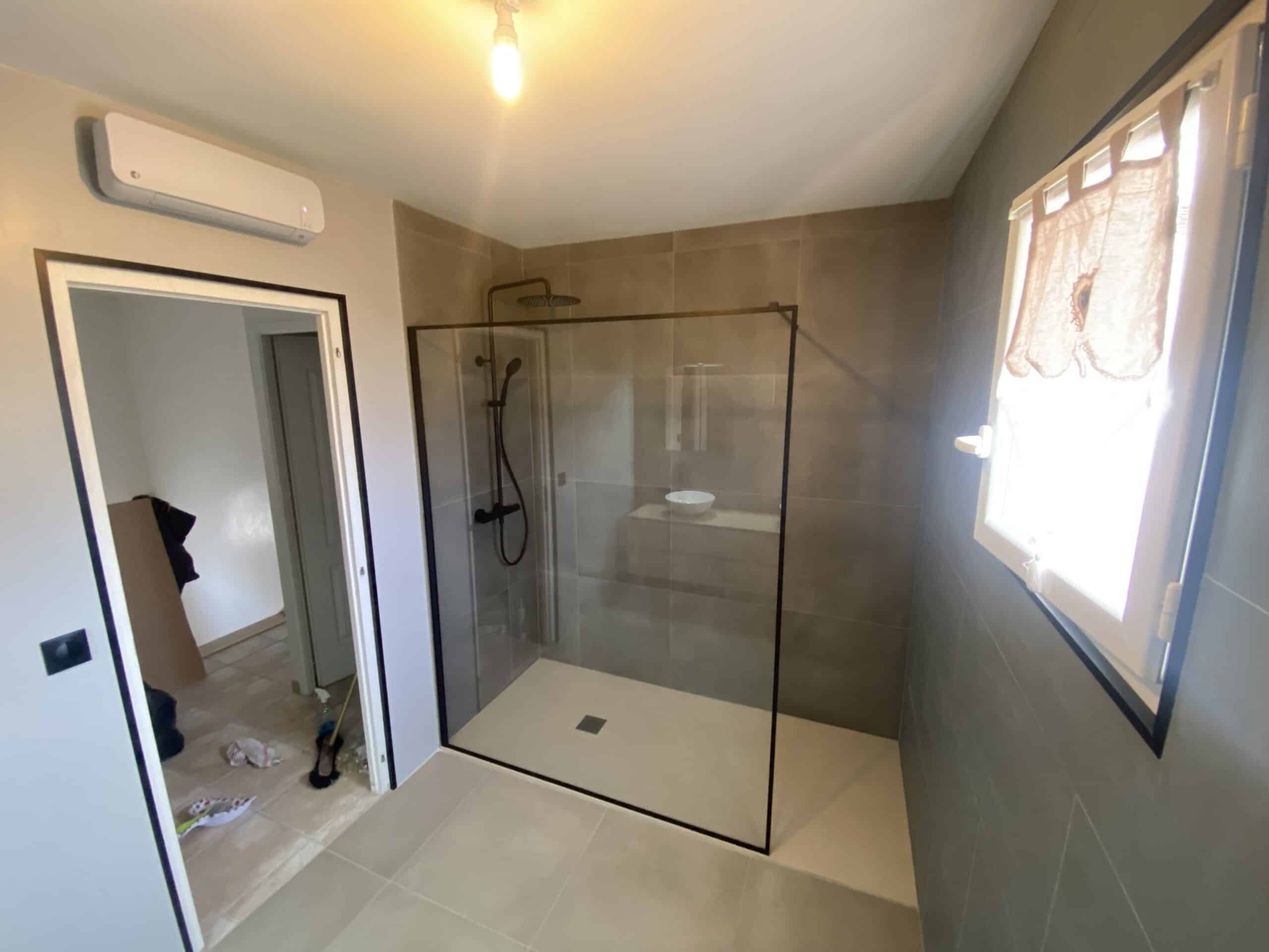 Salle de bain moderne en rénovation. Grande douche italienne avec profilés noirs, robinetterie mate et carrelage grand format taupe.